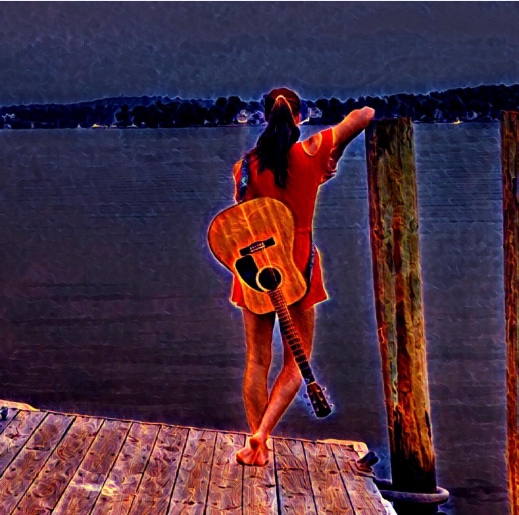 Rita Kay with guitar on a dock at sunset